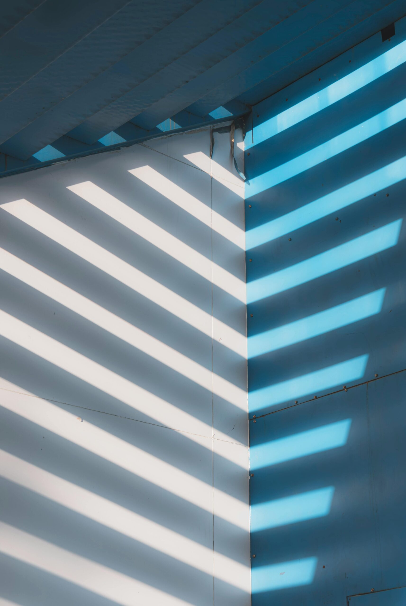 Diagonal light and shadow pattern on a blue wall, creating an abstract visual effect.